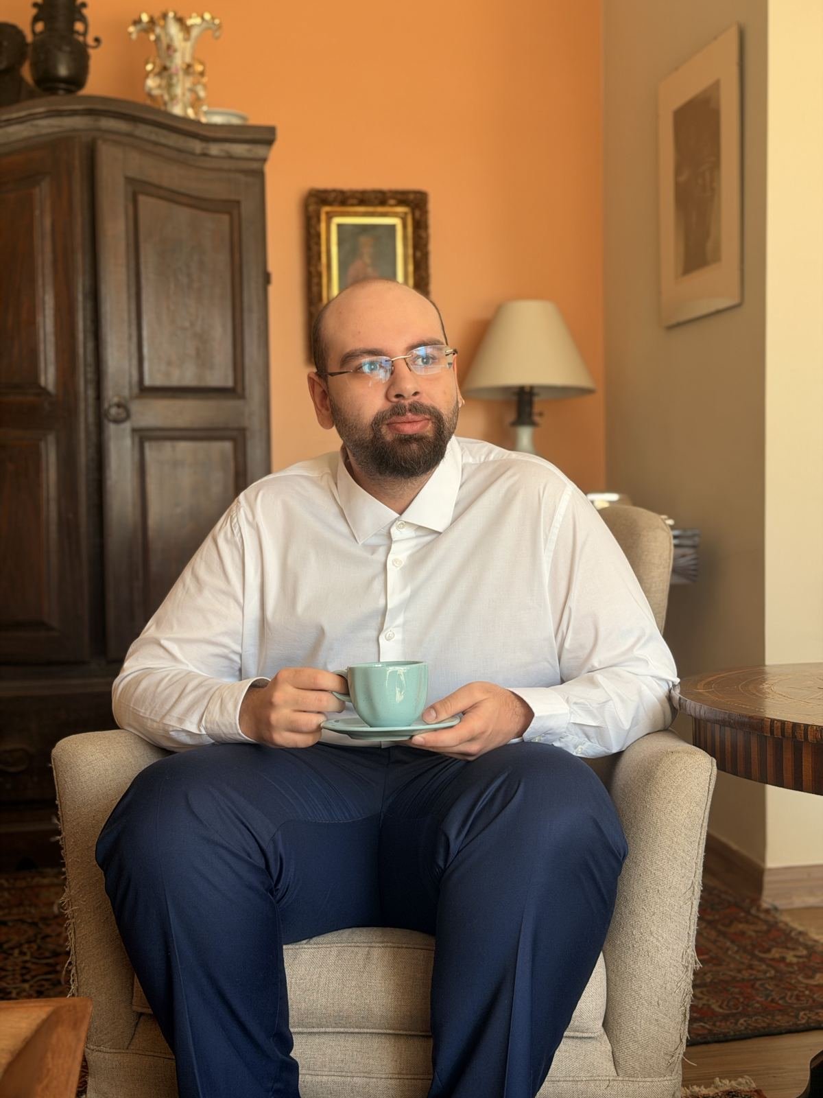 João Guilherme Falavigna segurando uma xícara, sentado em uma poltrona